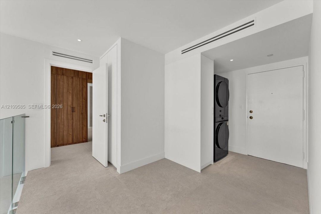 Stacked laundry unit, full-height wood-finish cabinetry, recessed ceiling lighting, and glass panel railing