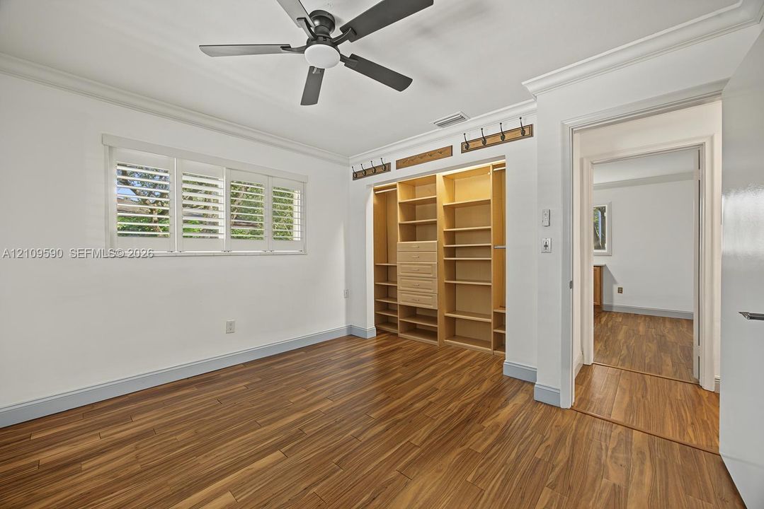 Bedroom 4 - Wood-finish flooring, custom built-in cabinetry, adjustable interior window shutters, ceiling fan, and crown molding