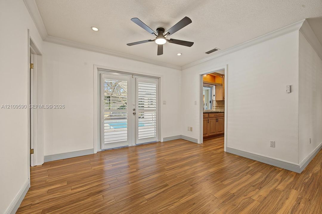 Room featuring wood-finish flooring, crown molding, ceiling-mounted light fixture with fan, and double glass doors with built-in shutters