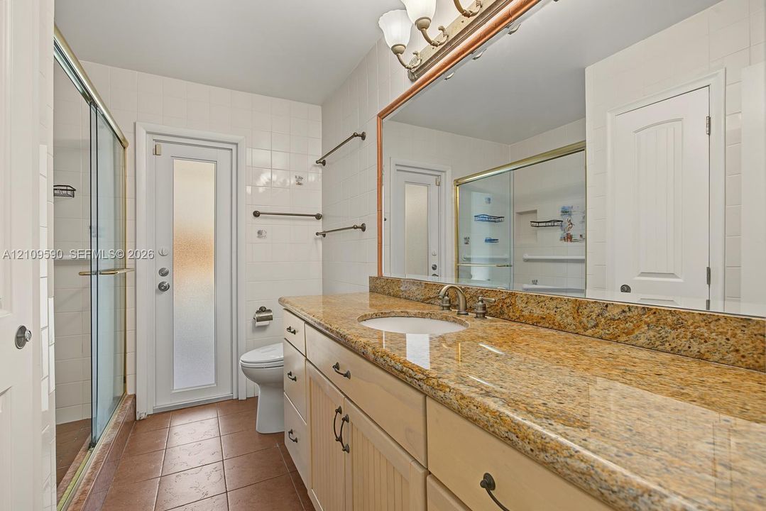 Bathroom featuring a vanity with stone countertop, drop-in sink, wood-finish cabinetry, a glass-enclosed shower, and tile flooring