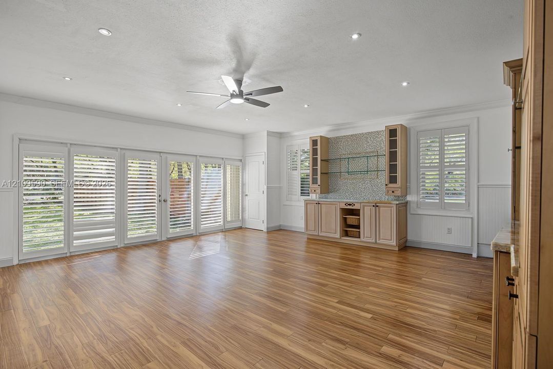 Living area featuring wood-finish flooring, recessed lighting, a ceiling fan, a set of multi-panel sliding doors with integrated shutters, and built-in cabinetry with glass shelving and a mosaic tile backsplash