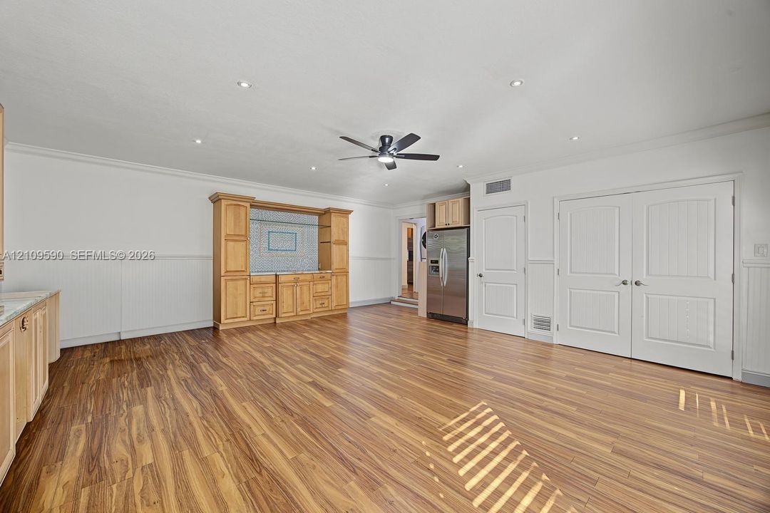 Open floor plan featuring wood-finish flooring, built-in wooden cabinetry with tiled backsplash, recessed ceiling lighting, a central ceiling fan, and double panel doors