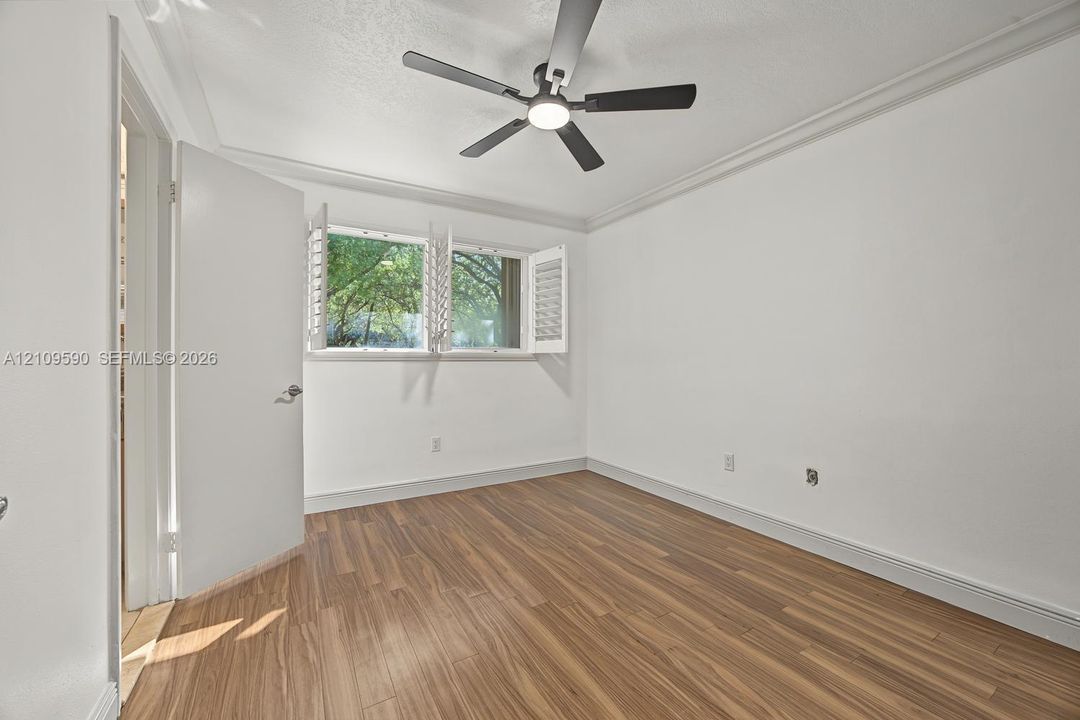 Bedroom 2 - Room featuring wood-finish flooring, crown molding, a ceiling fan with integrated lighting, and operable louvered window shutters