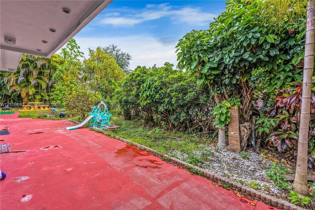 Outdoor space featuring a covered patio, paved hardscaping, established trees, and perimeter foliage