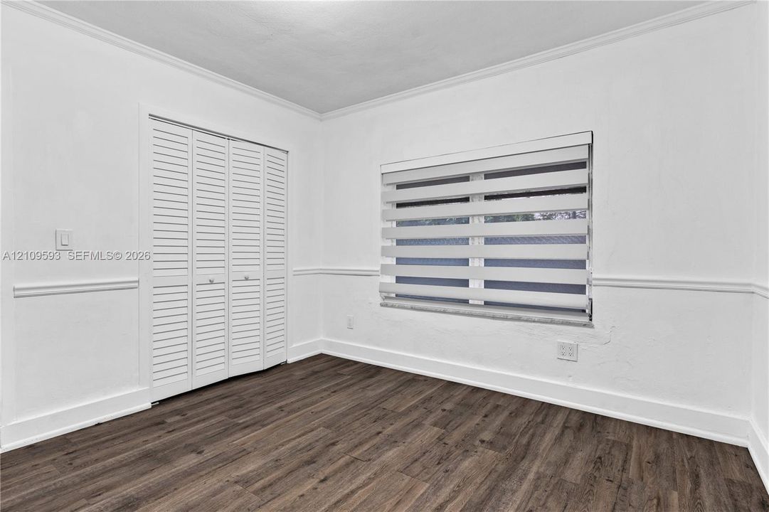 Room featuring wood-finish flooring, white louvered-style closet doors, neutral wall molding, and dual-layered adjustable window shades