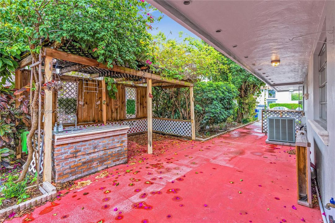 Covered patio featuring a brick-base bar, wood-frame trellis, stone-surfaced countertop, and lattice privacy screening