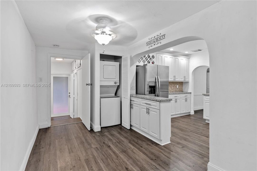 White cabinetry with brushed nickel hardware, stone-finish countertops, stainless steel appliances, wood-finish flooring, and built-in laundry area with stacked washer and dryer