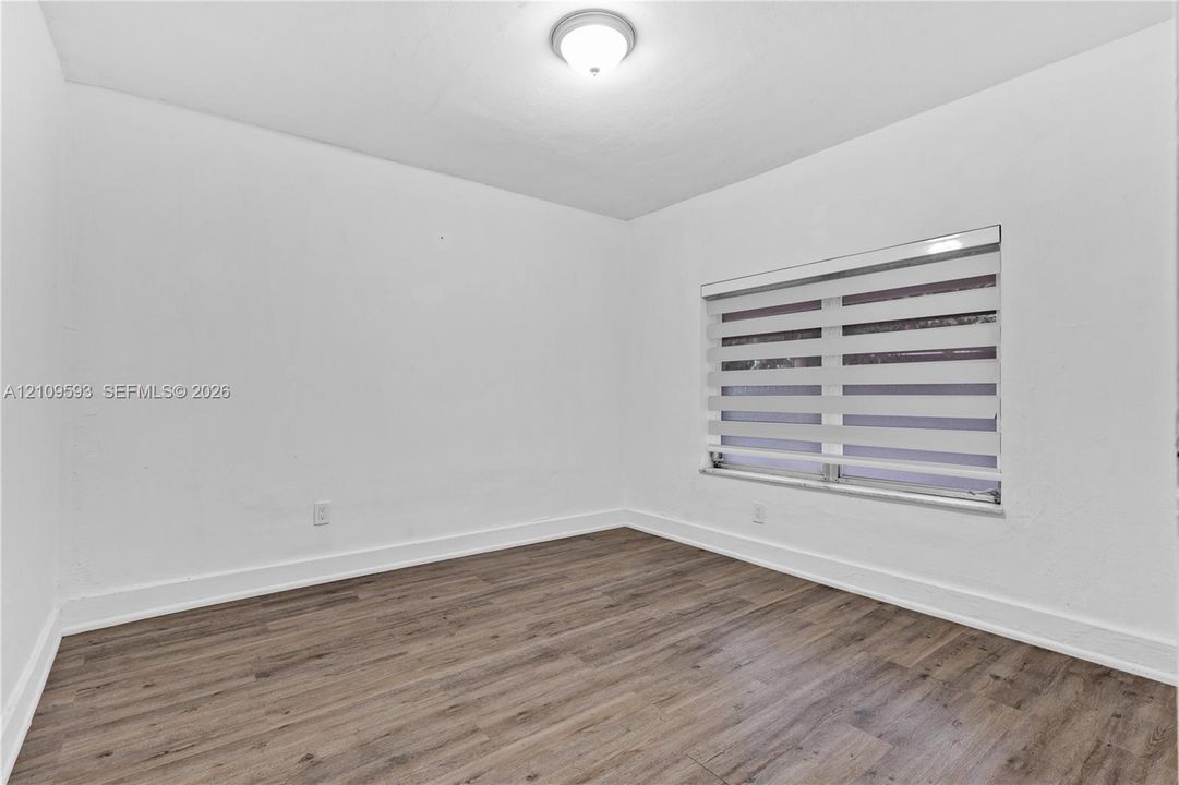 Room featuring wood-finish flooring, white walls, flush-mount ceiling lighting, and a single window with adjustable horizontal shades
