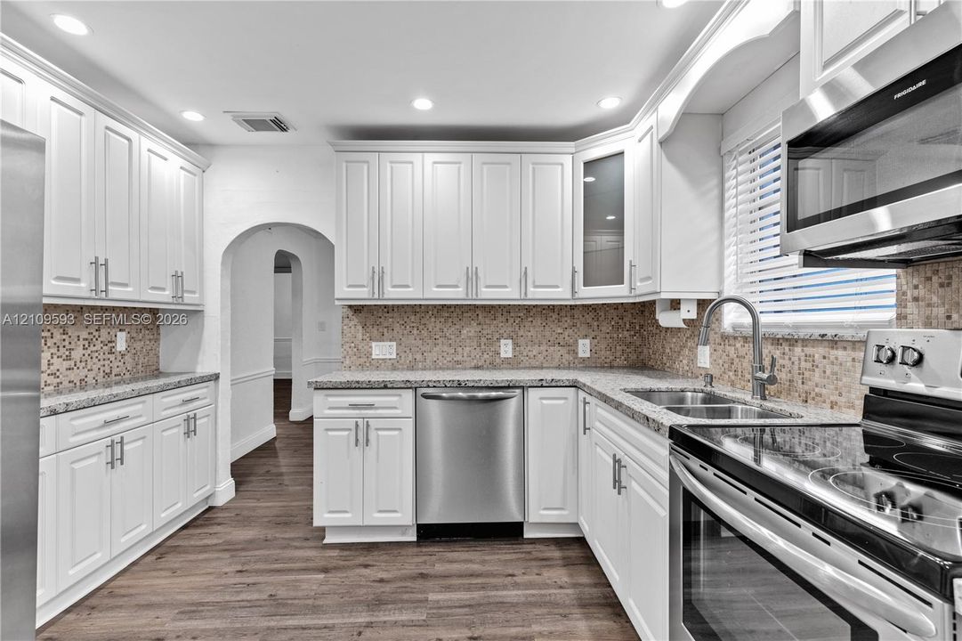 Kitchen featuring white shaker-style cabinetry, stone-finish countertops, mosaic tile backsplash, stainless steel appliances, and wood-finish flooring