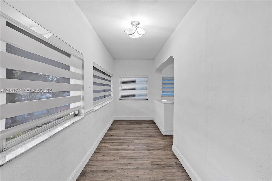 Interior space featuring wood-finish flooring, dual-tone roller shades, stone window sills, arched architectural pass-through, and a ceiling-mounted light fixture
