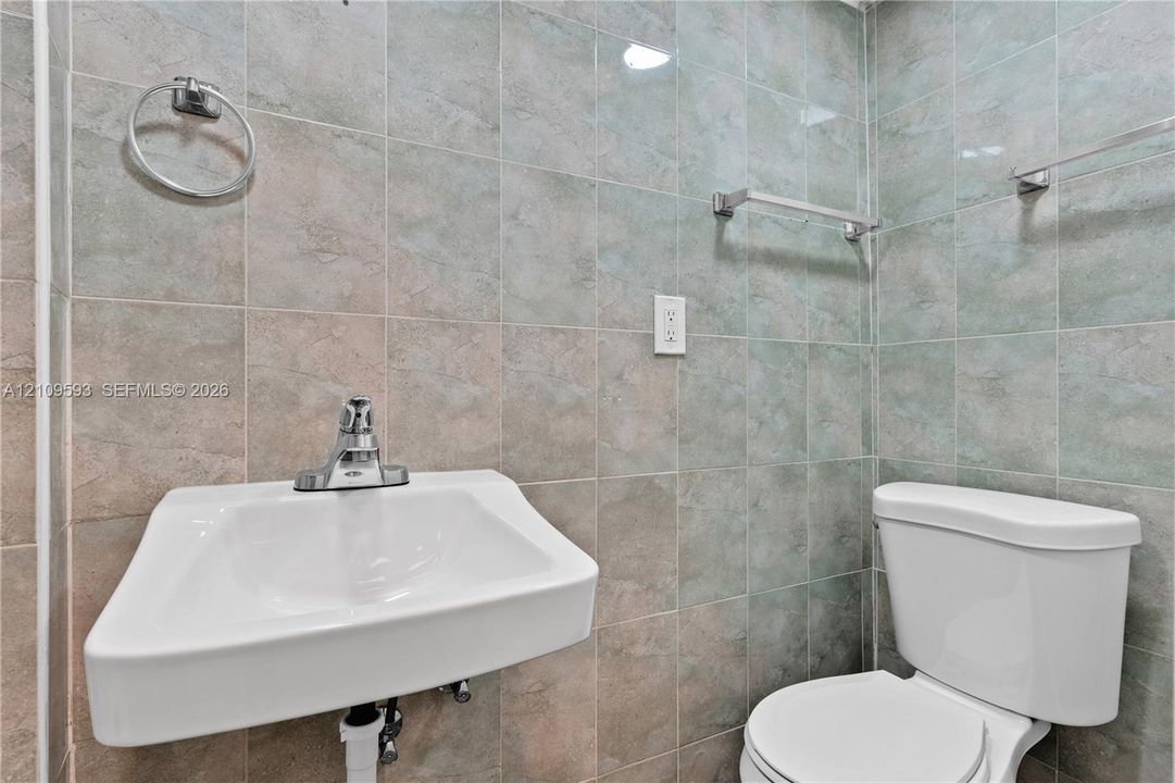 Wall-mounted sink with a chrome finish faucet, complemented by floor-to-ceiling stone-finish wall tiling, a two-piece toilet, and polished chrome hardware