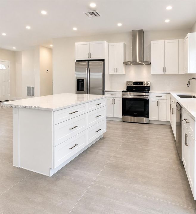 Kitchen featuring white shaker-style cabinetry, a central island with storage drawers, light-toned stone-finish countertops, stainless steel appliances, and large-format neutral-tone tile flooring