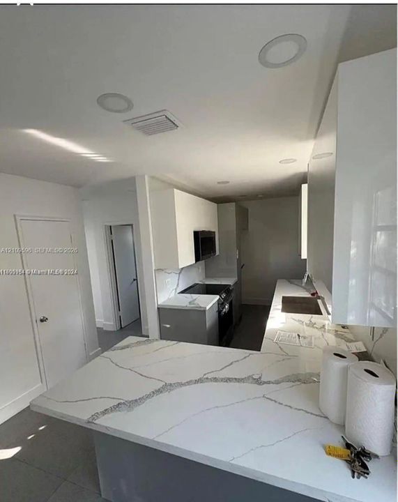 Kitchen featuring high-gloss white upper cabinetry, grey base cabinets, stone-finish countertops with veining, and recessed ceiling lighting