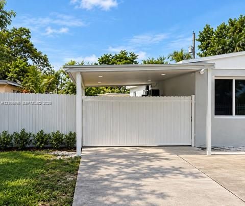 Covered carport featuring integrated recessed lighting, concrete driveway, and full-height privacy fencing with a motorized rolling gate