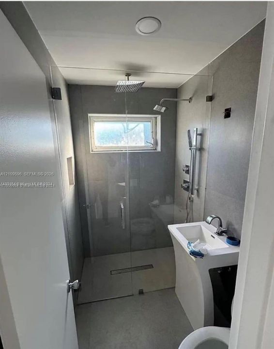 Walk-in shower with a glass enclosure, square rainfall showerhead, handheld shower fixture, recessed wall niche, and pedestal sink with a chrome faucet