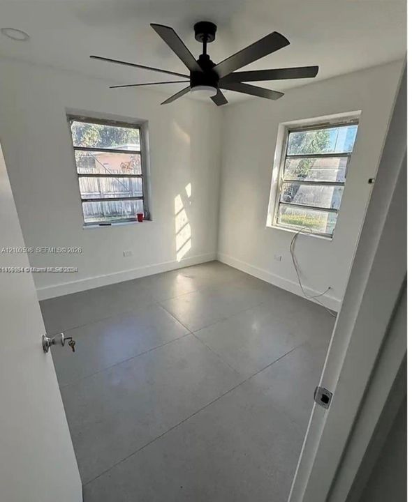 Room featuring large-format tile flooring, multi-pane windows, and a matte black ceiling fan