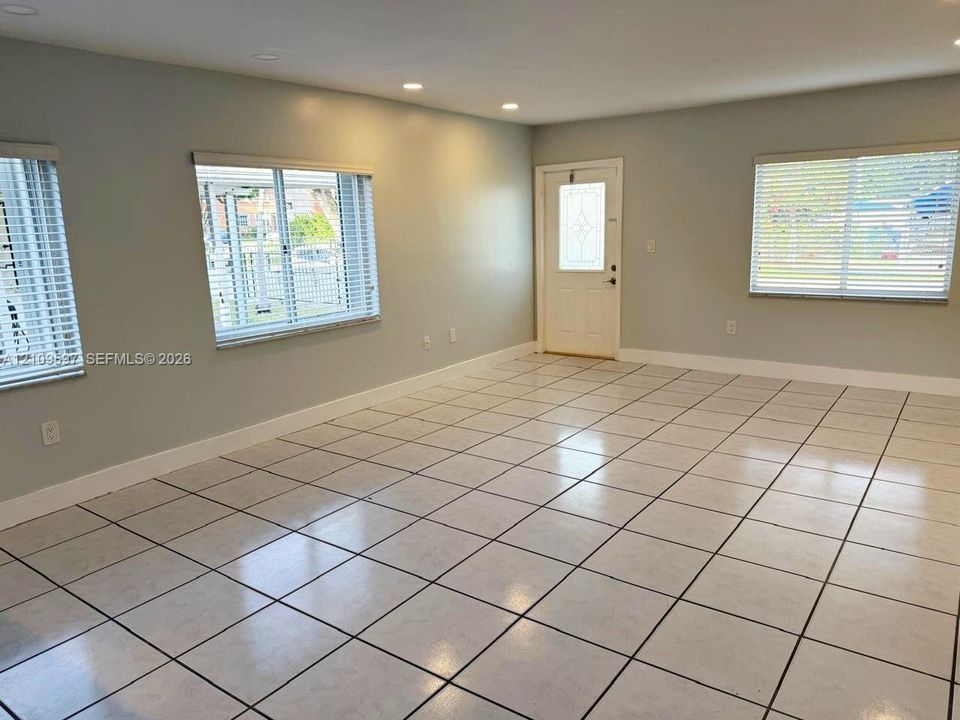Open-concept interior featuring large-format grid-pattern ceramic tile flooring, recessed ceiling lighting, and multiple windows with horizontal blinds