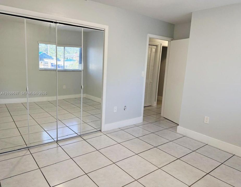 Light-colored ceramic tile flooring, floor-to-ceiling mirrored closet doors, and a window with a horizontal blind