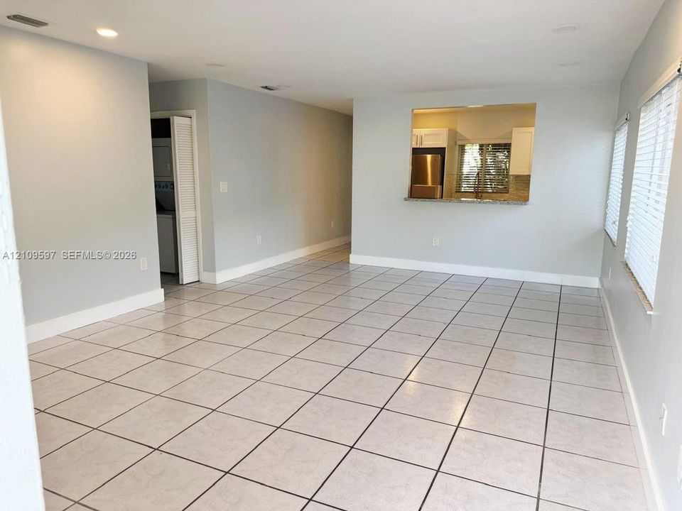 Neutral-toned interior featuring large-format ceramic tile flooring, recessed ceiling lighting, louvered closet doors, and a kitchen passthrough with a stone countertop