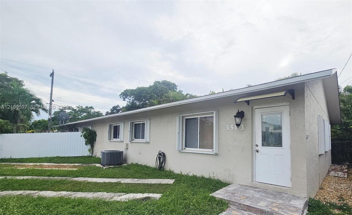 Single-story exterior featuring light-colored stucco siding, a shingled roof, sliding windows with white frames, a white entry door with a decorative glass inset, and stone-finish porch tiles