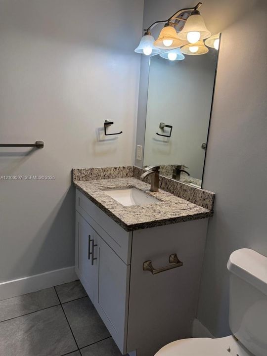 Vanity featuring a stone-composite countertop, undermount sink, brushed-nickel hardware, integrated wall mirror, and multi-bulb overhead vanity lighting