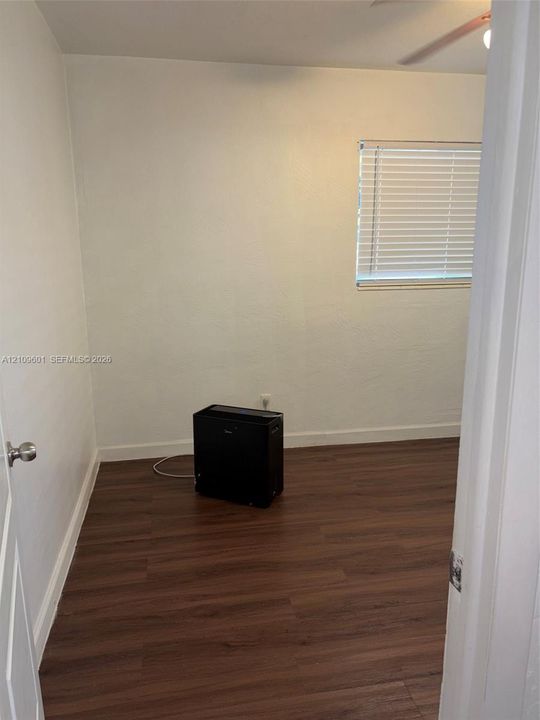 Room featuring wood-finish flooring, smooth white walls, and a window fitted with horizontal blinds