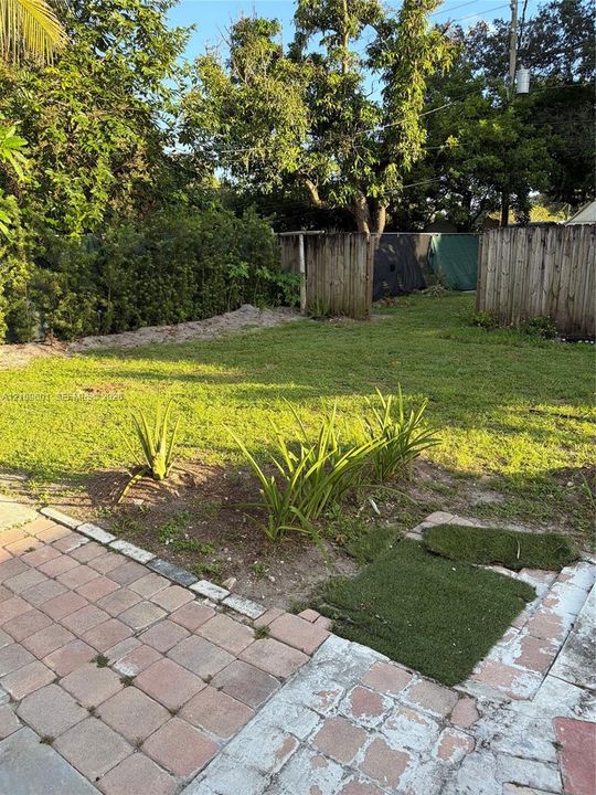 Backyard featuring a paved brick patio, grassy lawn, mature trees, wood privacy fencing, and established ground plantings