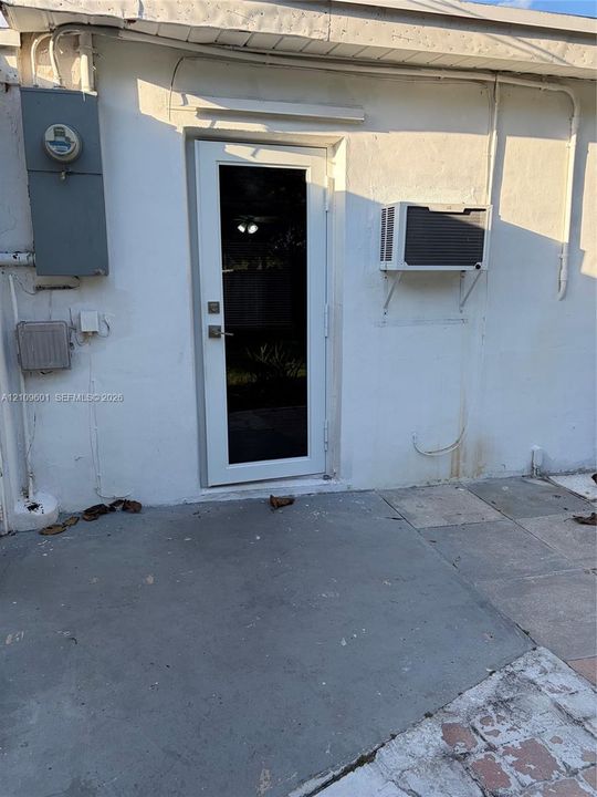 Exterior entry featuring a glass-panel door, concrete patio surface, and a wall-mounted cooling unit