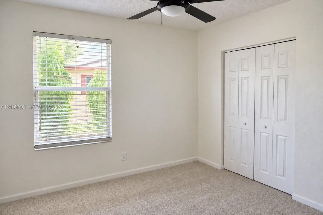 Room featuring neutral wall-to-wall carpeting, a double-panel bi-fold closet, a single-hung window with horizontal blinds, and a central ceiling fan with integrated lighting