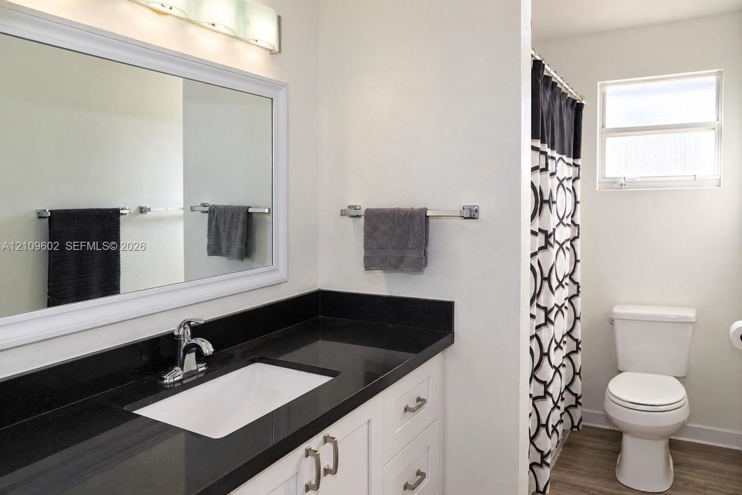 Bathroom featuring white cabinetry, a dark countertop with an integrated basin, a large wall-mounted mirror, and wood-finish flooring