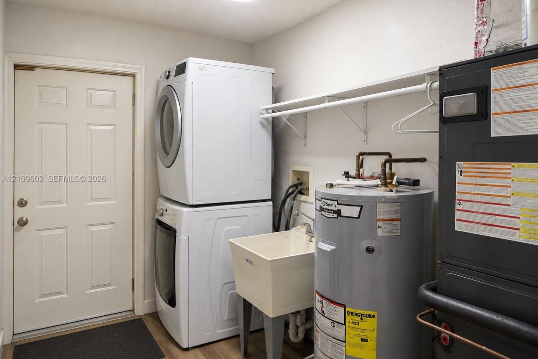 Utility area featuring a built-in wash basin, stackable laundry unit, integrated shelving, and water heating system