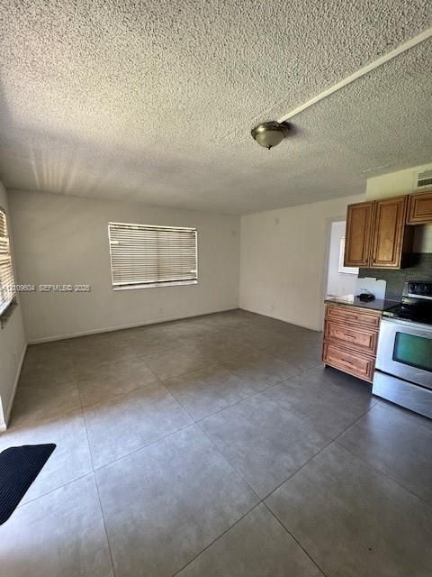Large-format tile flooring, wood cabinetry, stainless steel oven, and window blinds