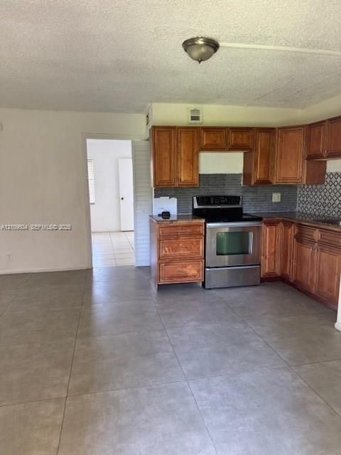 Kitchen featuring wood cabinetry, stone countertops, decorative tile backsplash, stainless steel range, and large-format tile flooring