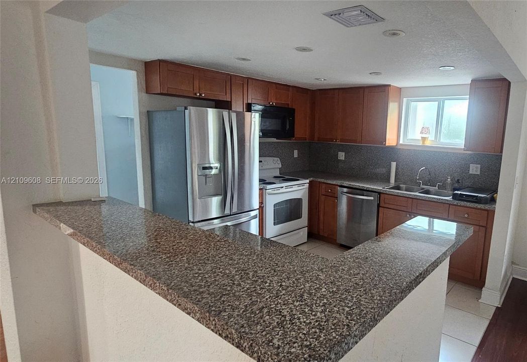 Kitchen featuring stained wood cabinetry, stone-finish countertops, stainless steel appliances, a peninsula breakfast bar, and recessed lighting