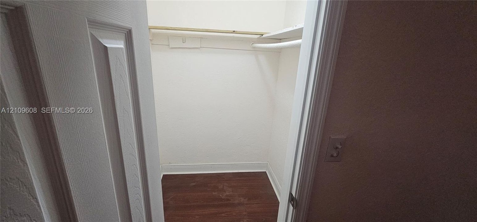 Storage closet featuring wood-finish flooring, a built-in shelf, and an integrated hanging rod
