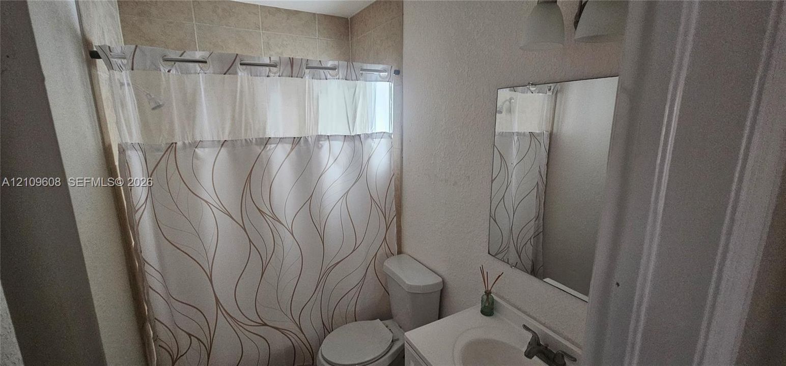 Bathroom featuring a neutral tile shower surround, wall-mounted vanity with integrated sink, rectangular mirror, and dual-bulb overhead lighting fixture