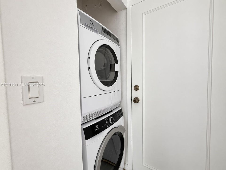 Stacked white front-load washer and dryer set with metallic trim, situated within a recessed laundry alcove featuring a solid-core white door with dual metallic hardware