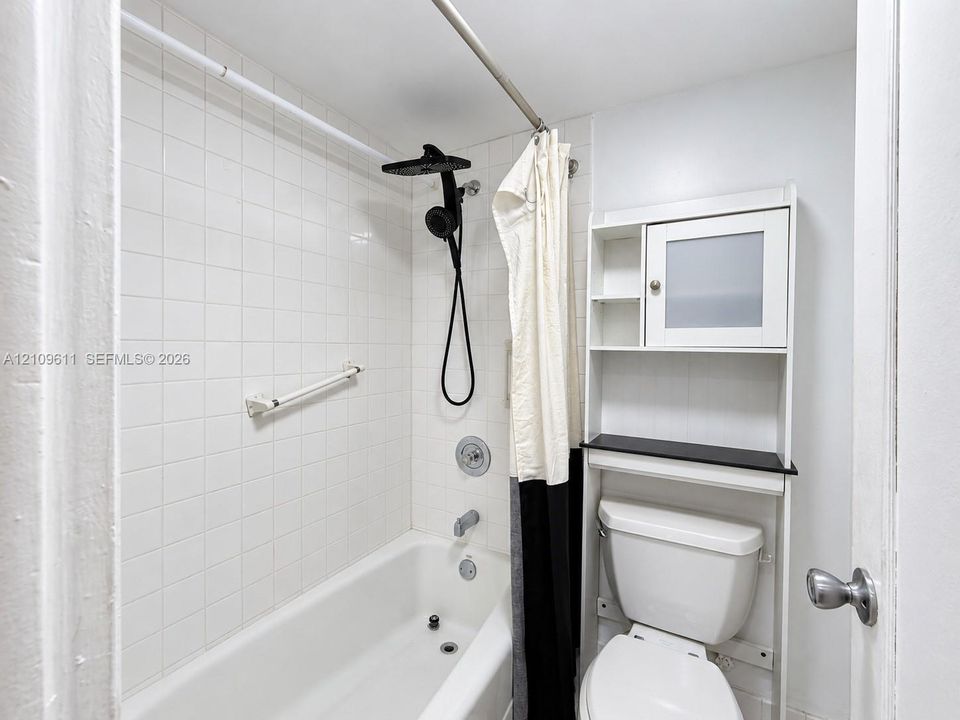 Full-size bathtub with white wall tile surround, black rainfall shower head, and integrated grab bar