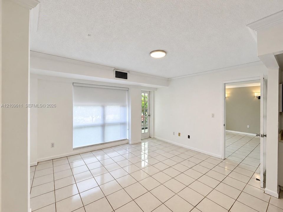 Interior space featuring large-format ceramic tile flooring, neutral wall finishes, crown molding, a multi-pane glass door, and a built-in recessed ceiling light fixture