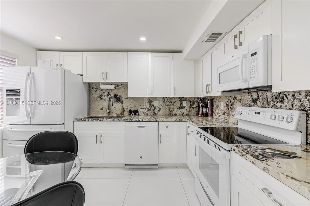 Kitchen featuring white cabinetry, stone countertops, stone backsplash, large-format tile flooring, and white appliances