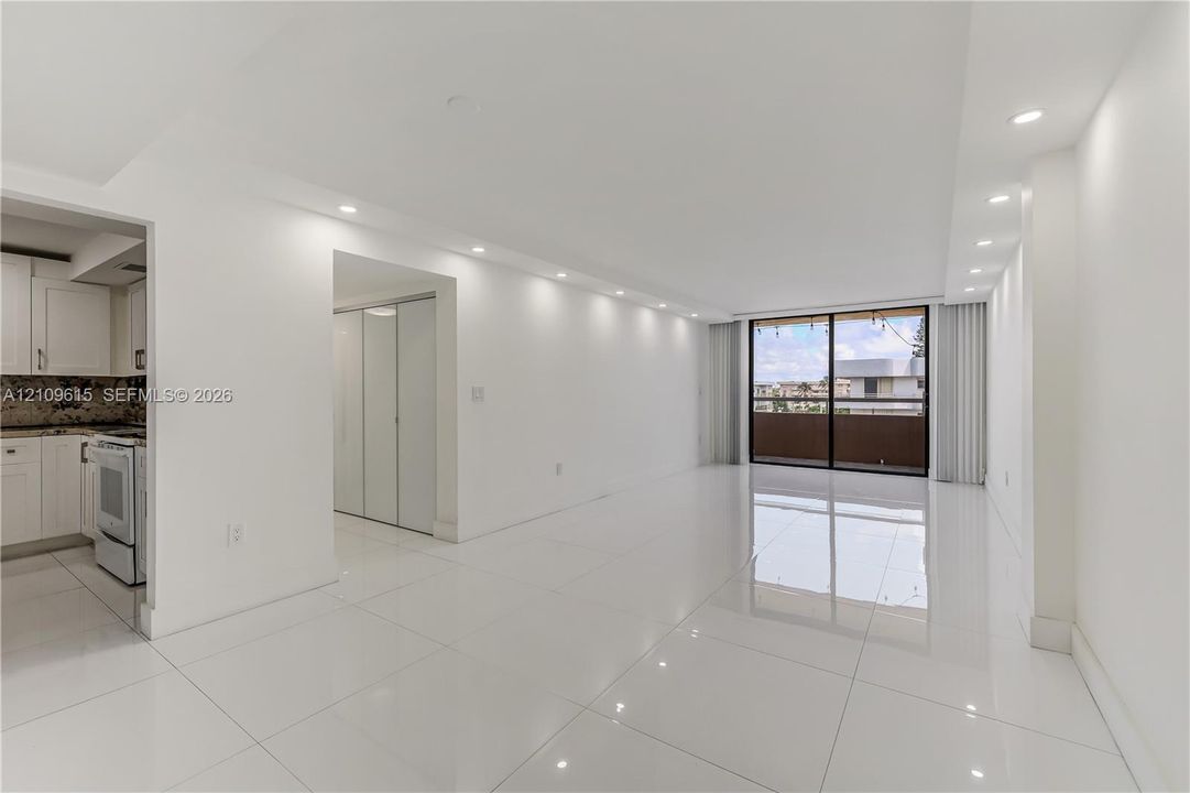 Open-concept interior featuring polished tile flooring, recessed ceiling lighting, sliding glass balcony doors, and built-in closet cabinetry