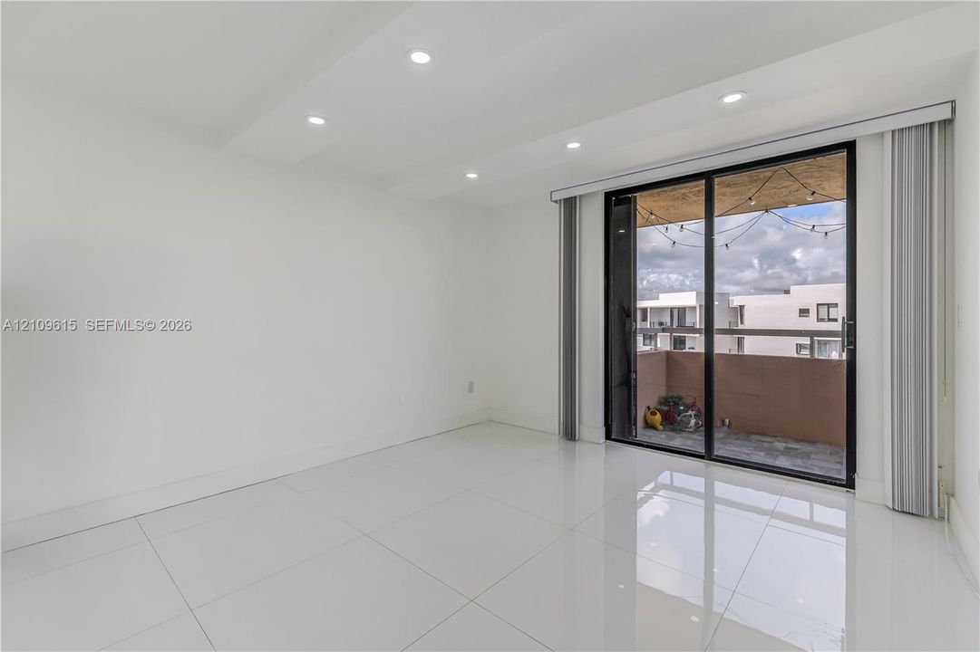 Interior space featuring high-gloss tile flooring, recessed ceiling lighting, and sliding glass doors leading to a balcony with metal railings
