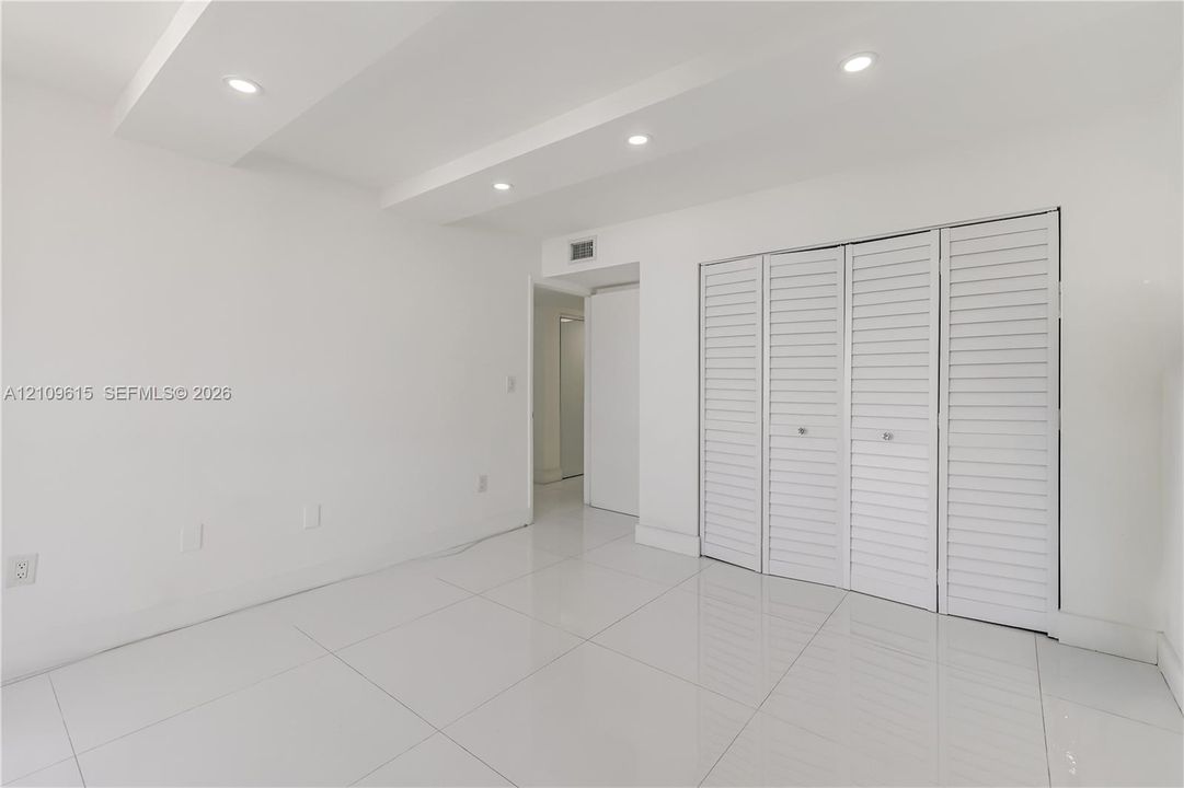 Polished tile flooring, recessed ceiling lighting, and built-in closet with louvered doors
