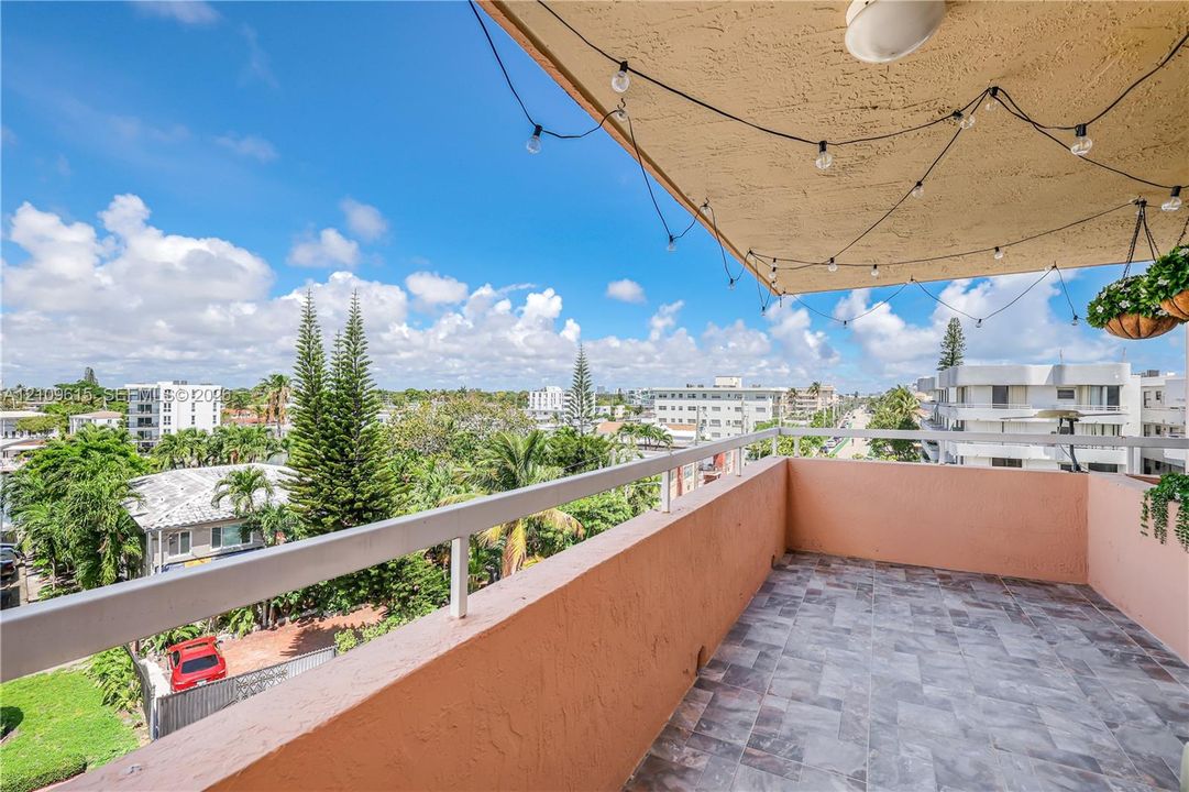 Covered balcony featuring stone-tile flooring, solid stucco walls, and a metal railing