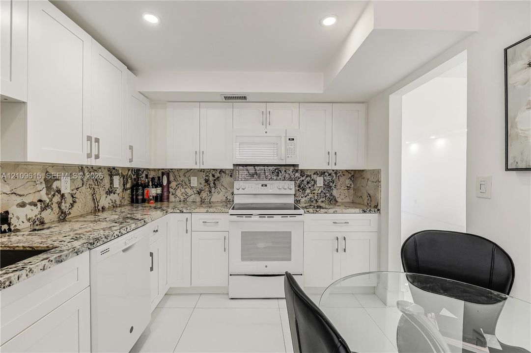 Kitchen featuring white cabinetry, stone-finish countertops and backsplash, integrated white appliances, and large-format tile flooring