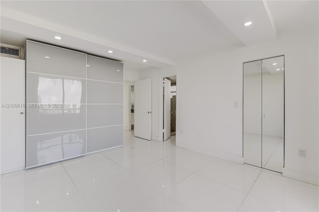 Large format white tile flooring, glossy sliding panel storage cabinetry, and mirrored bifold closet doors under recessed ceiling lighting