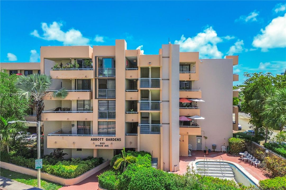 Multi-story exterior featuring concrete masonry construction, private balconies with metal railings, integrated ground-level pool, and mature tropical landscaping