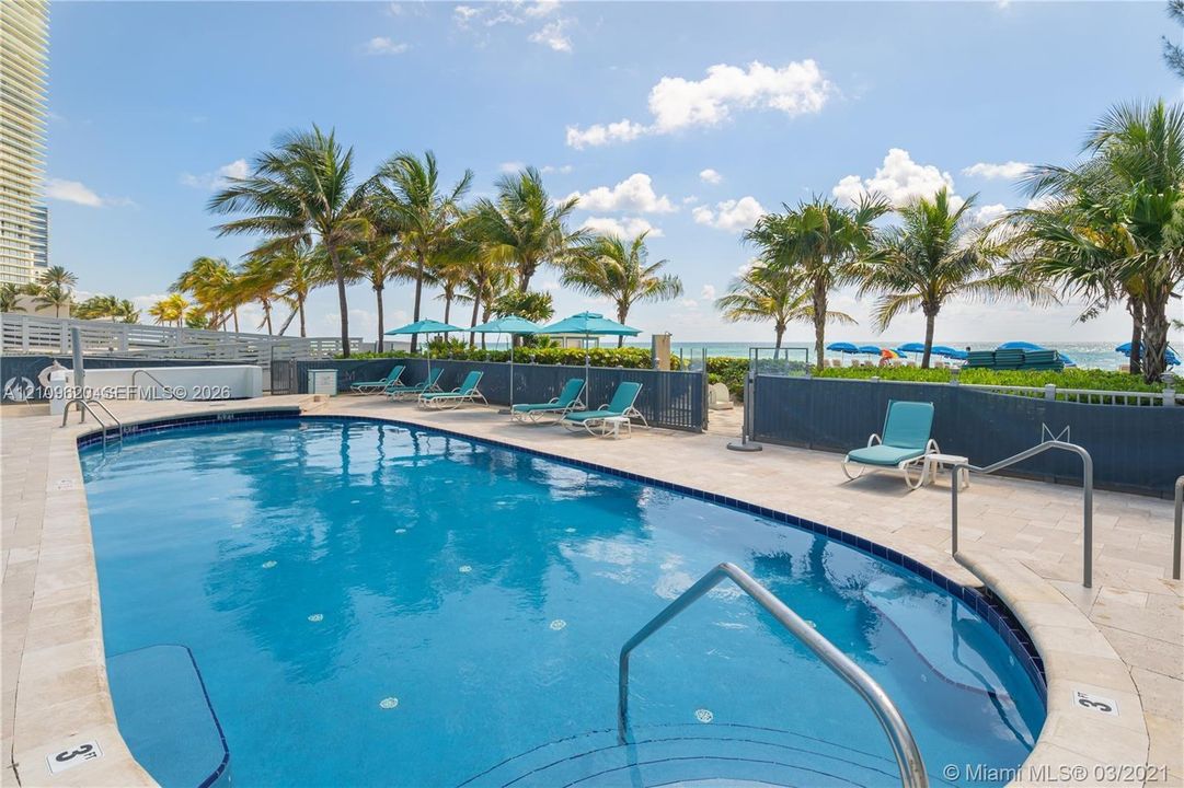 Swimming pool with stone-tiled decking, metal safety railings, and perimeter fencing