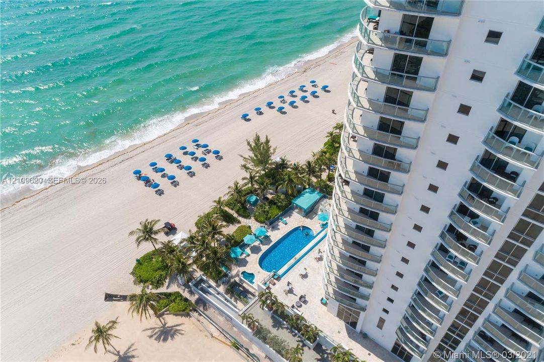High-rise residential building featuring expansive private balconies, a ground-level swimming pool, integrated hardscaping, and immediate coastal access