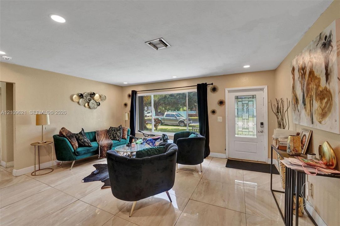 Large-format tile flooring, recessed ceiling lighting, and an expansive window providing natural illumination, complemented by a front entry door with decorative glass paneling